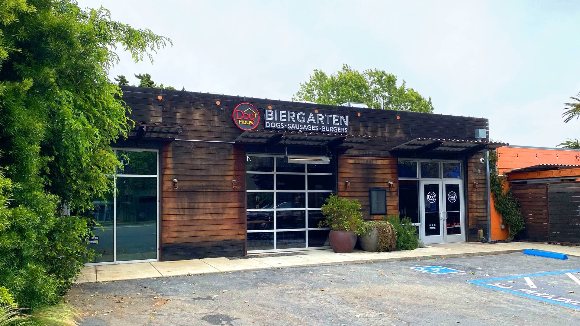 Exterior of Dog Haus Biergarten with wood-and-white facade, covered patio with string lights, and a curbside view under dramatic cloudy skies.