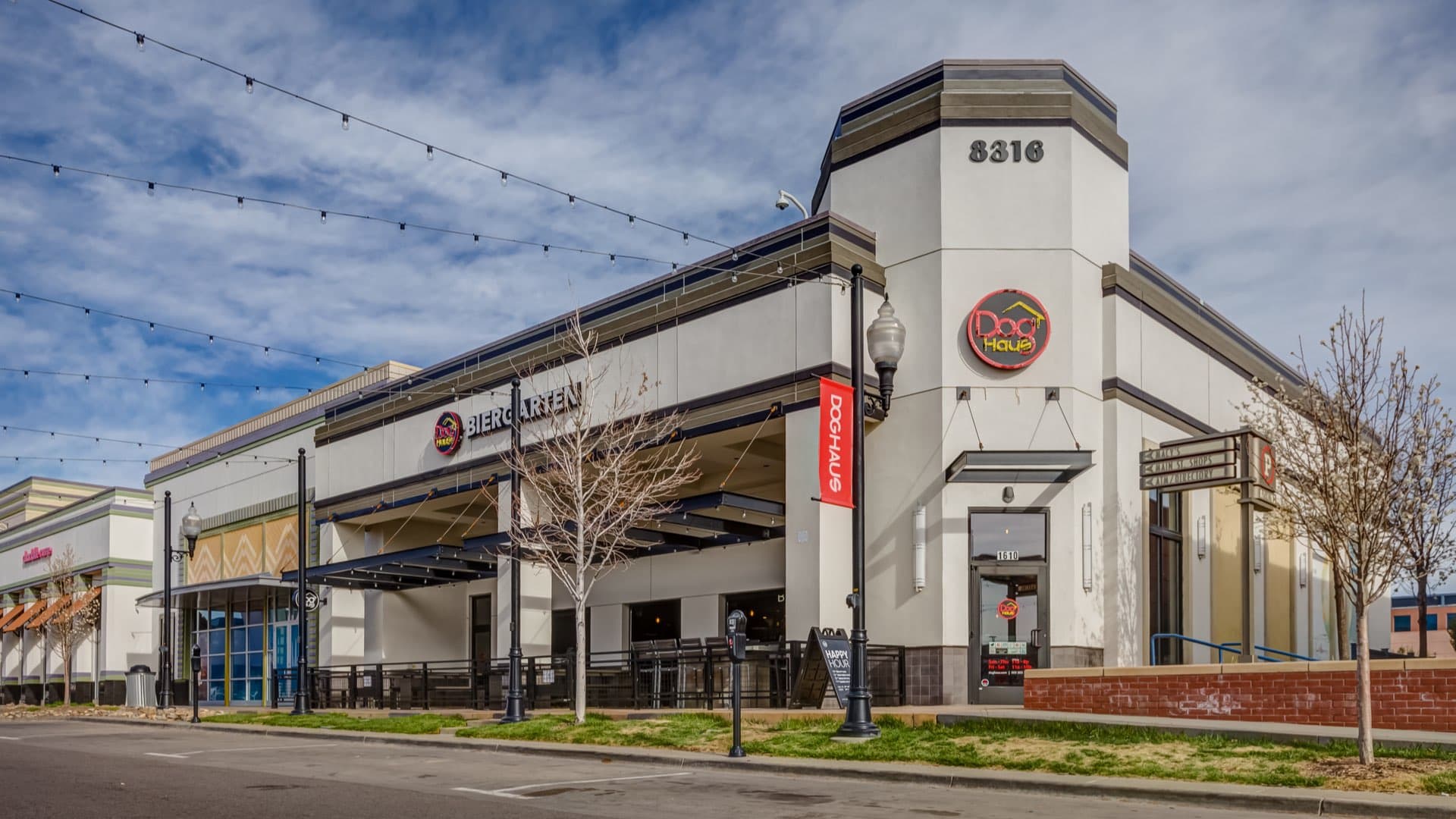 Exterior of Dog Haus Central Park with string lights, corner signage, and modern facade featuring patio seating and clear branding.