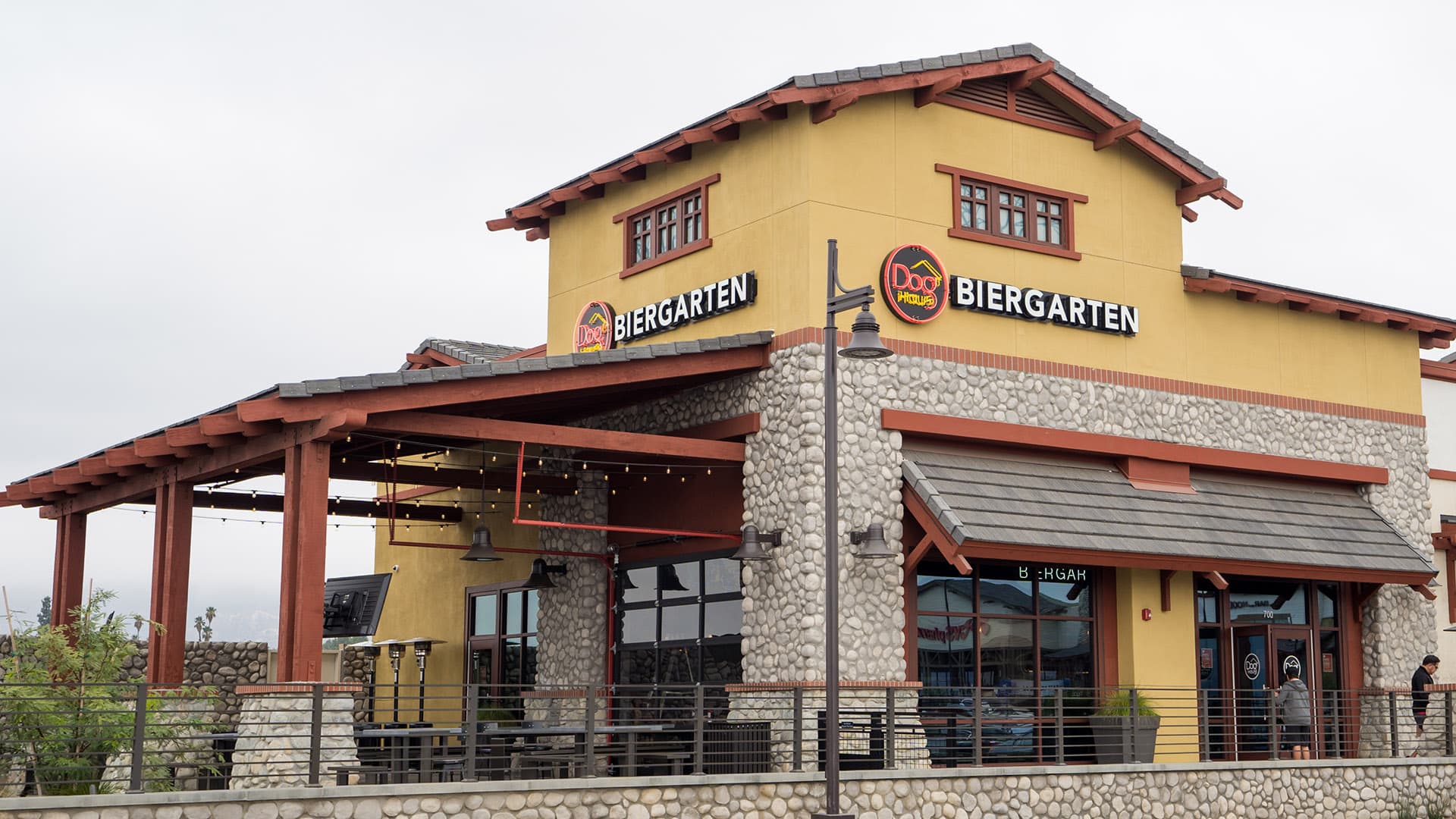Exterior of Dog Haus Biergarten Claremont with river rock walls, wood beam patio cover, and bold signage above the entrance.