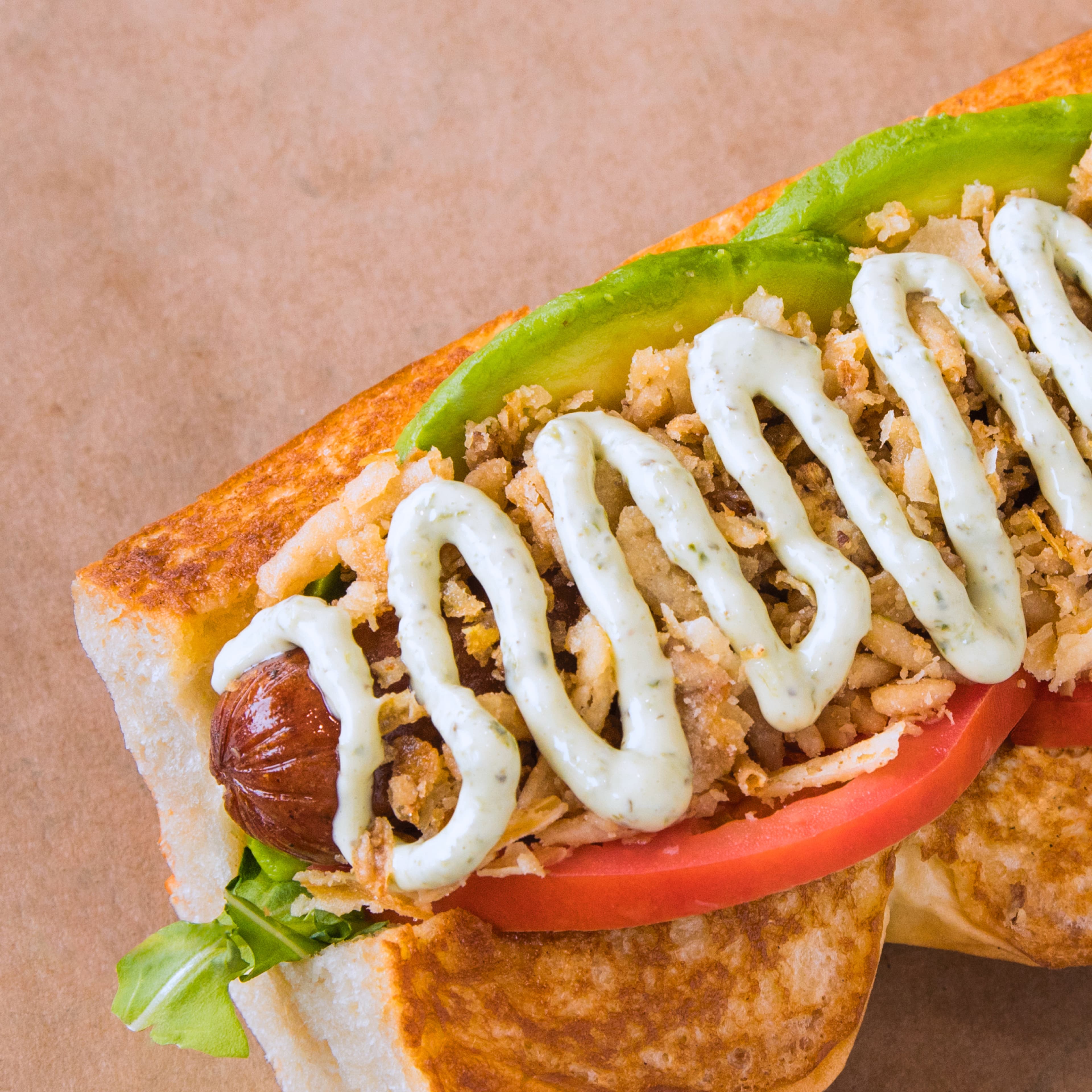 Hot dog topped with avocado, tomato, and crispy onions