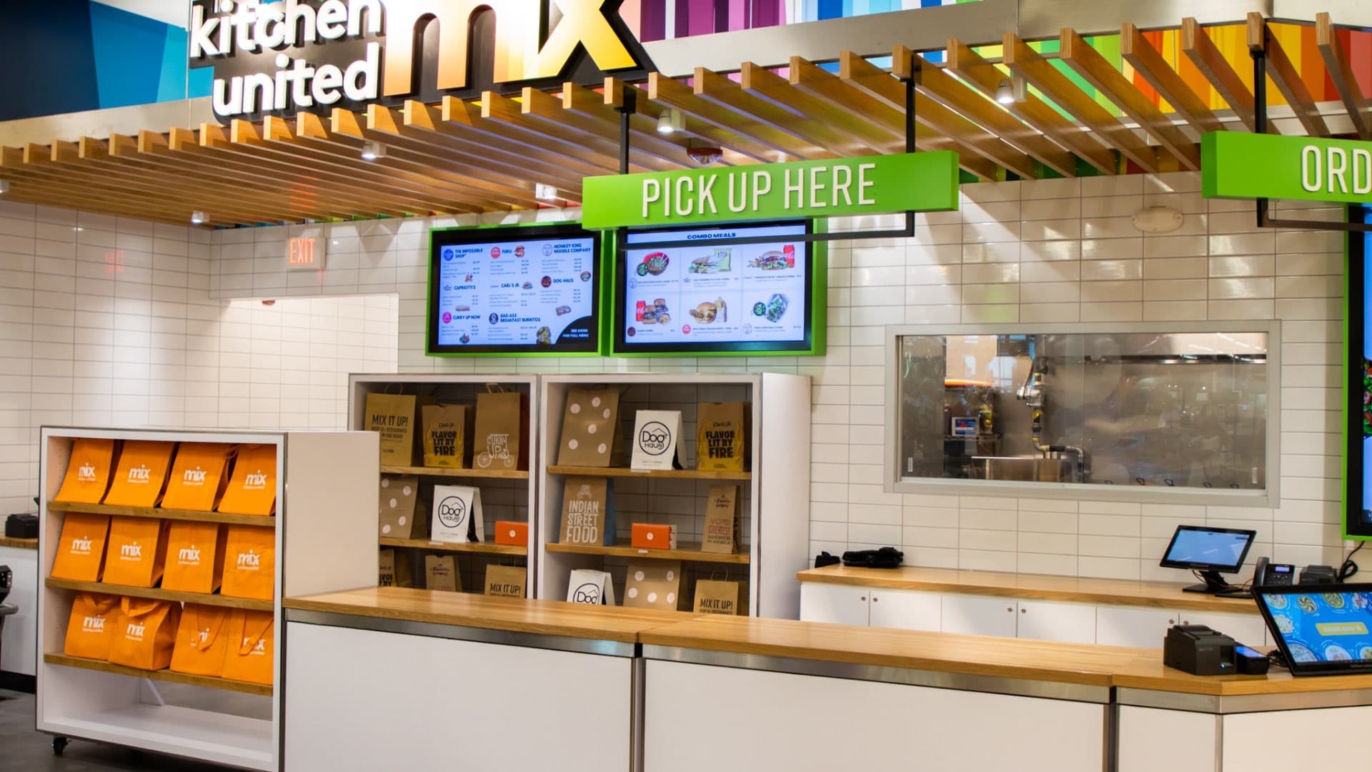 Interior view of Kitchen United Mix pickup station in Dallas, featuring Dog Haus branded bags, digital menu screens, and a clean white-tiled counter area
