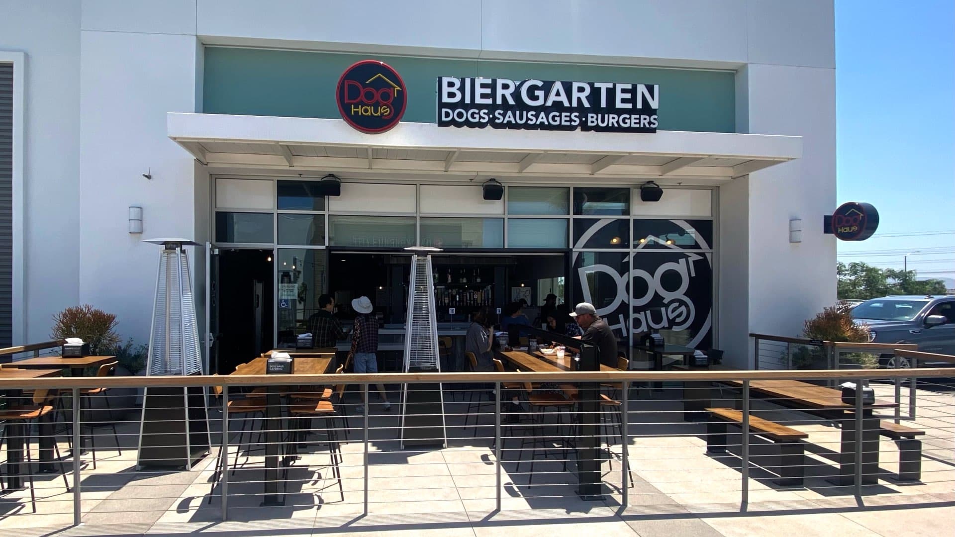 Exterior of Dog Haus Biergarten Eastvale featuring patio seating with tall heaters, large branded signage, and a modern storefront design.