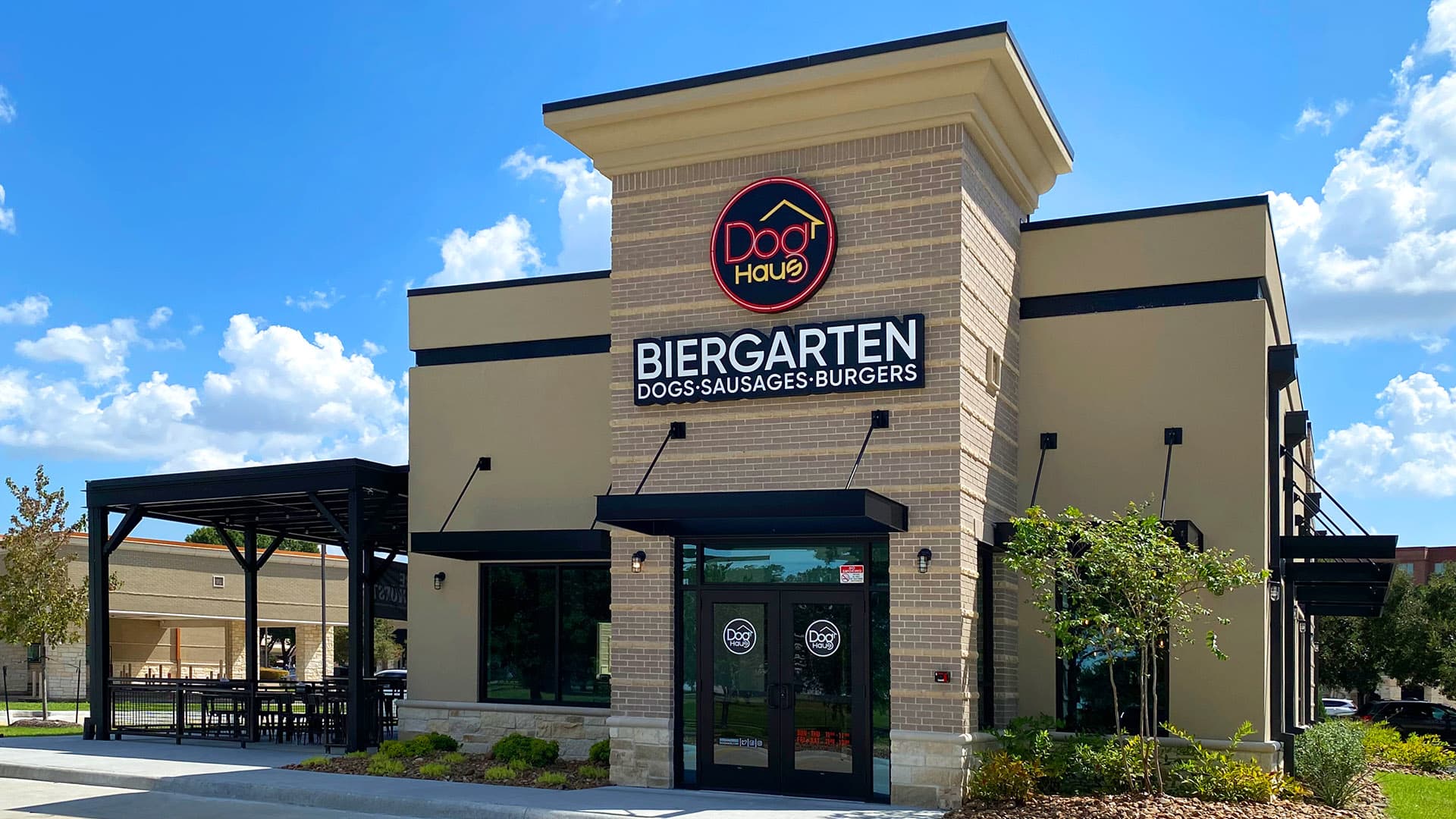 Front view of Dog Haus Biergarten Energy Corridor with large signage, brick and tan exterior, and a shaded entrance.