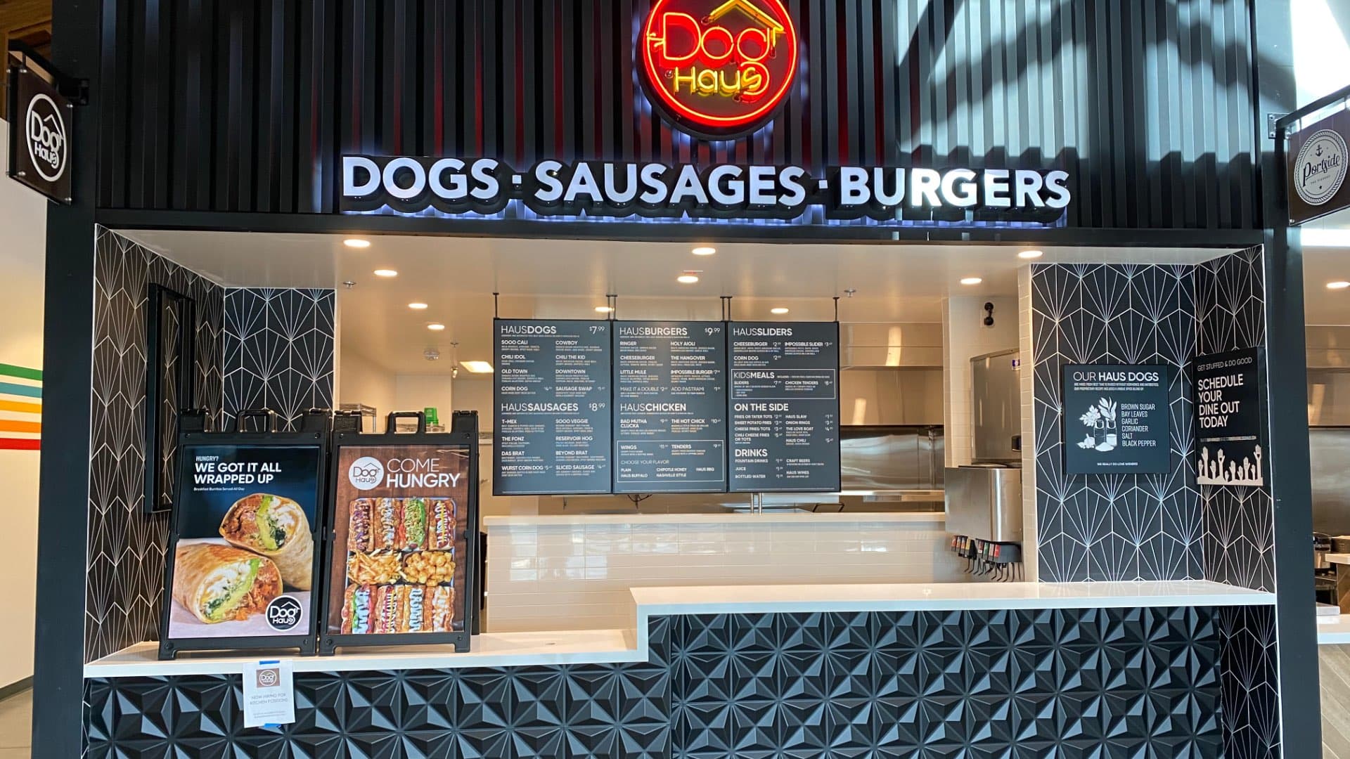 Front exterior of Dog Haus Fremont featuring bold signage for “Dogs, Sausages, Burgers,” black awnings, and customers waiting outside.