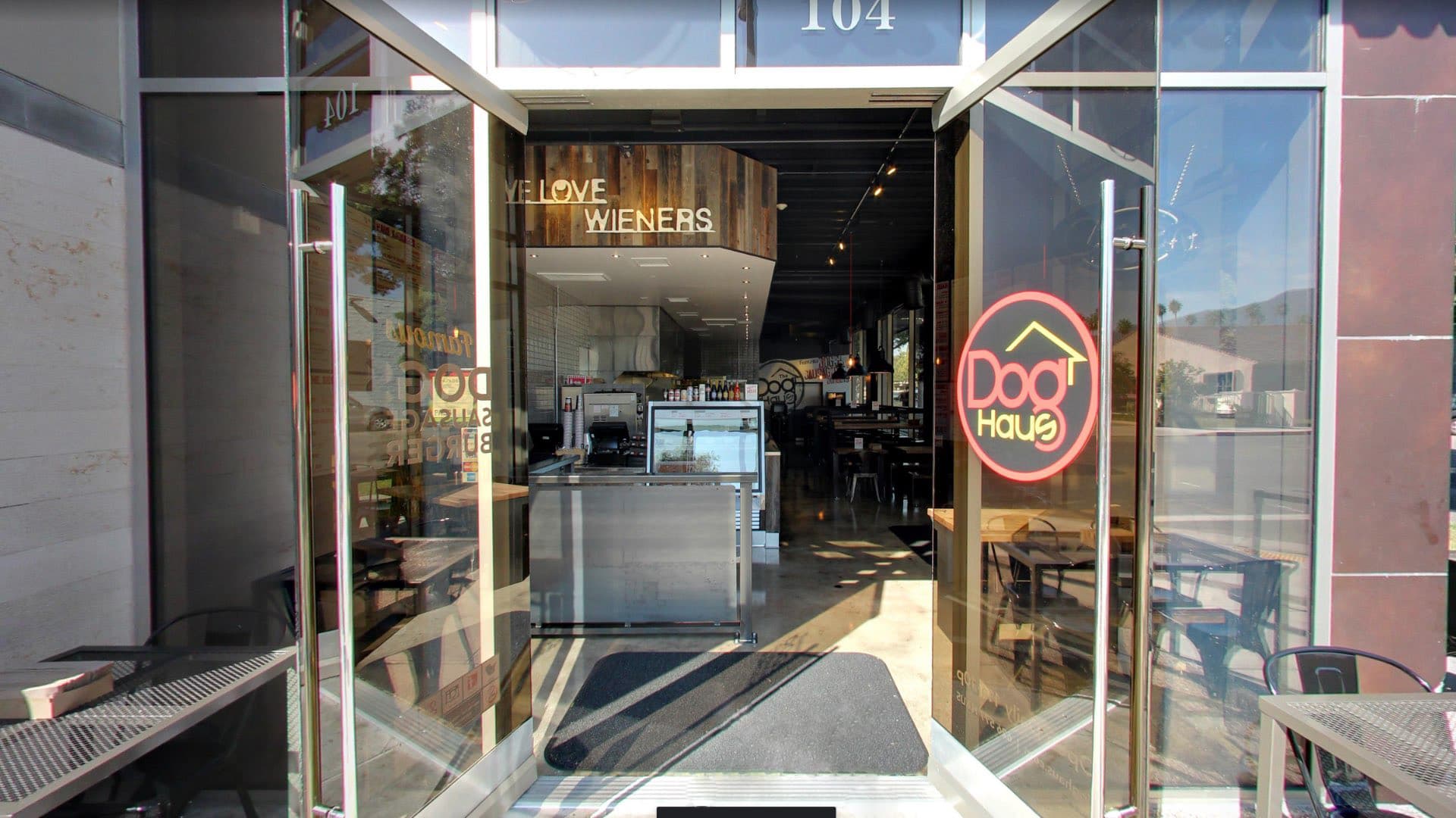 View from the entrance of Dog Haus Pasadena showing an open glass door leading into a modern interior with wood and metal finishes.