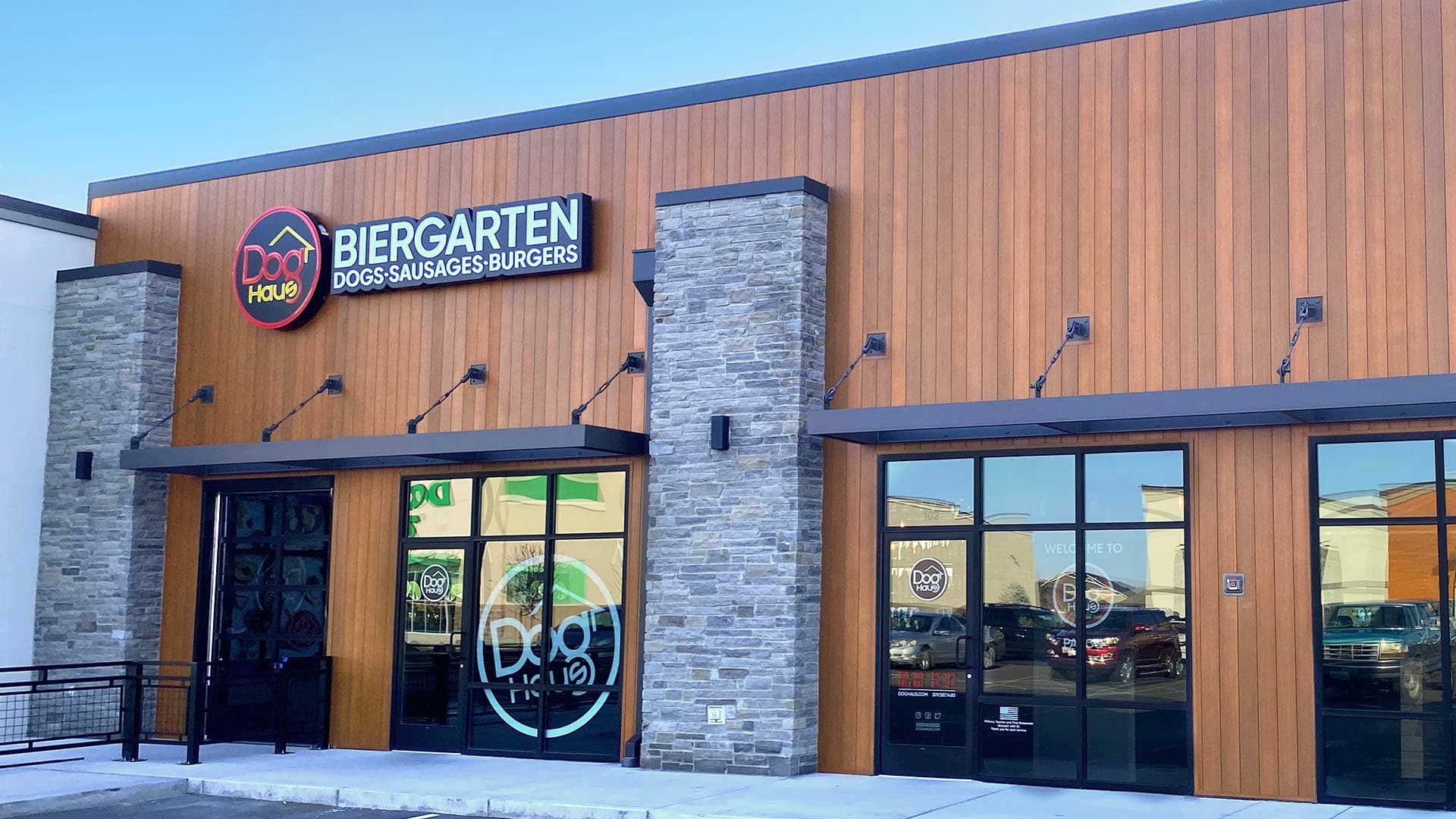 Exterior view of Dog Haus Biergarten Pasco, featuring modern wood-paneled facade, stone columns, and branded windows.