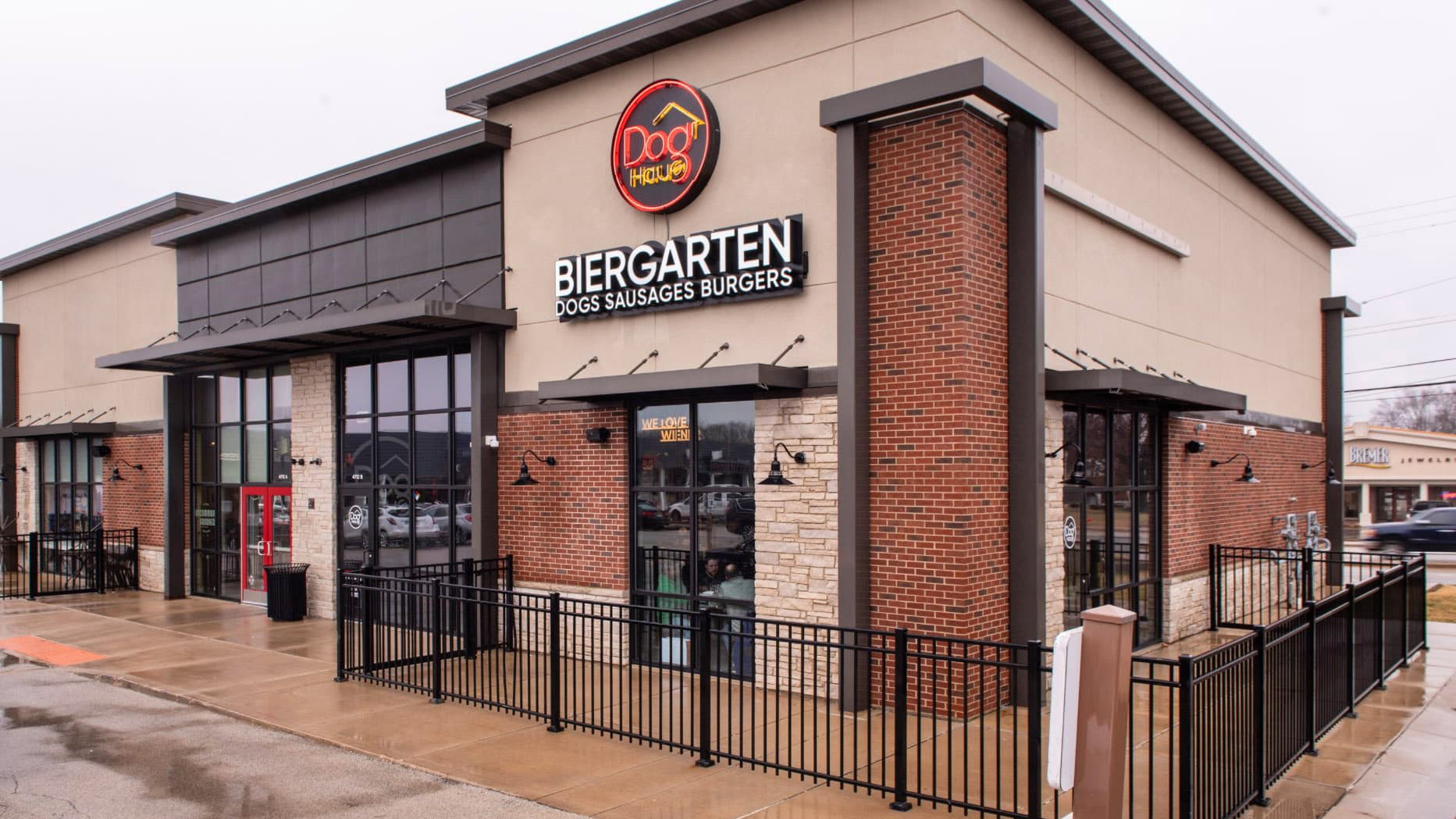 Exterior view of Dog Haus Biergarten Peoria, featuring modern brick and stone façade with bold signage and a fenced patio area.