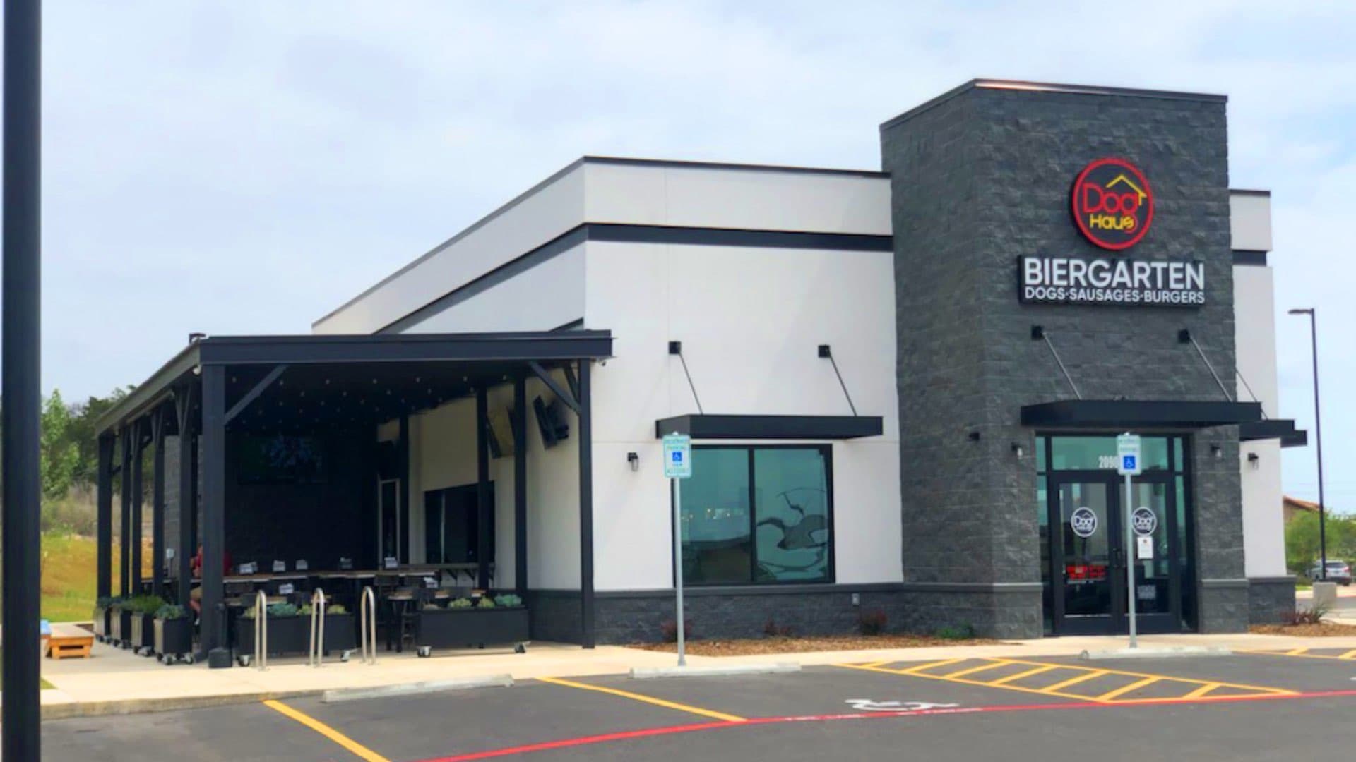A modern "Dog Haus Biergarten" restaurant building with white and dark stone siding, a prominent sign, and an attached outdoor patio.