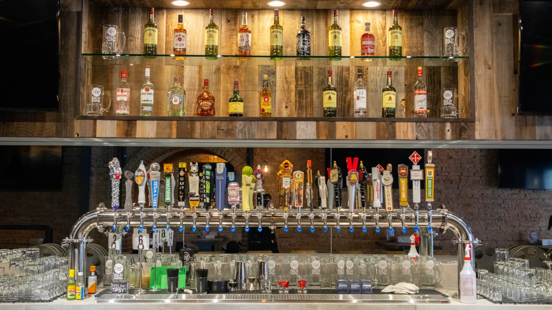 View of the Lincoln Park bar featuring a wide tap system, backlit liquor shelves, and exposed brick in the background.