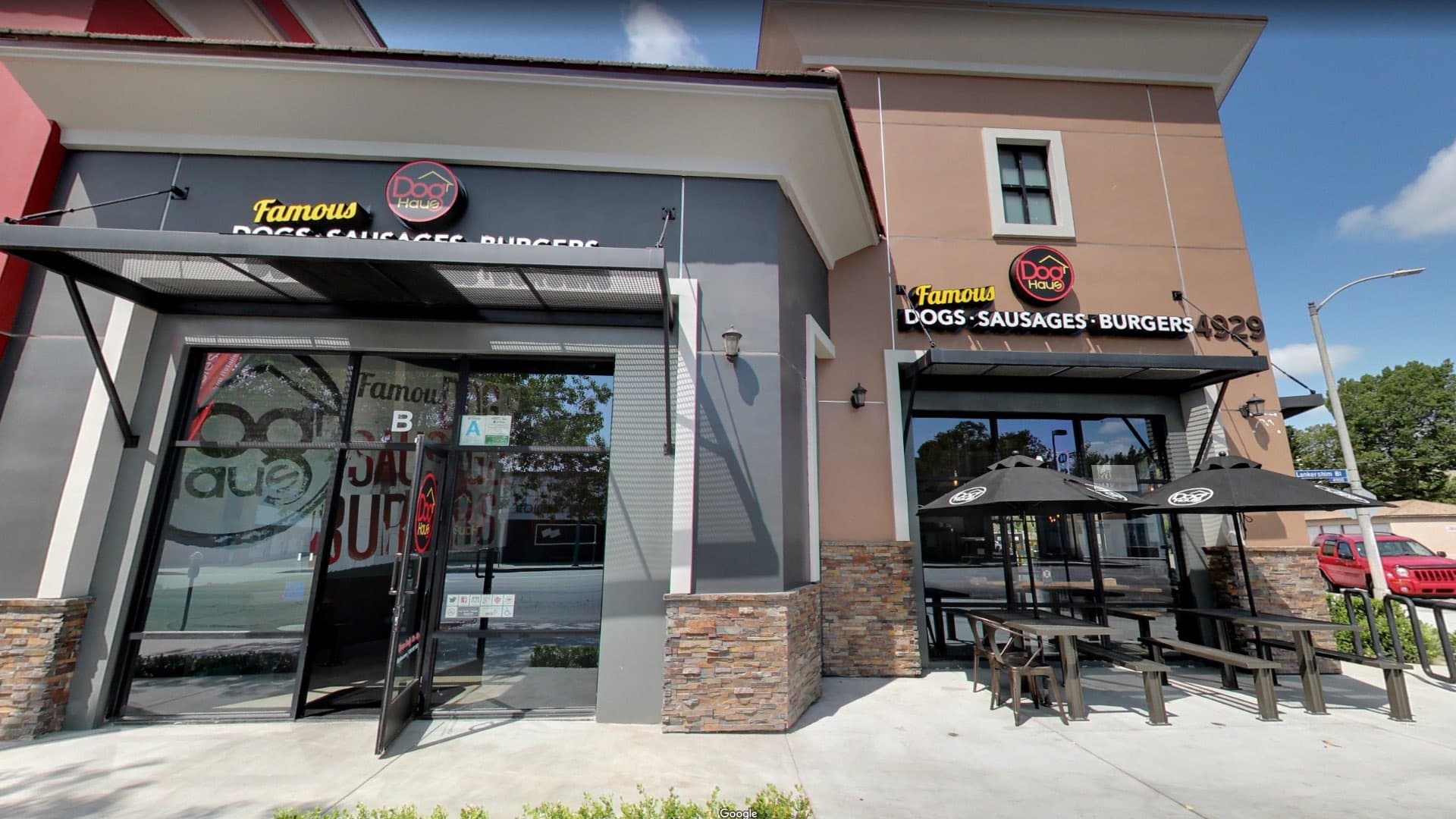 Exterior of Dog Haus NoHo with dual entrances, branded umbrellas, and outdoor patio seating under bold signage for sausages and burgers.