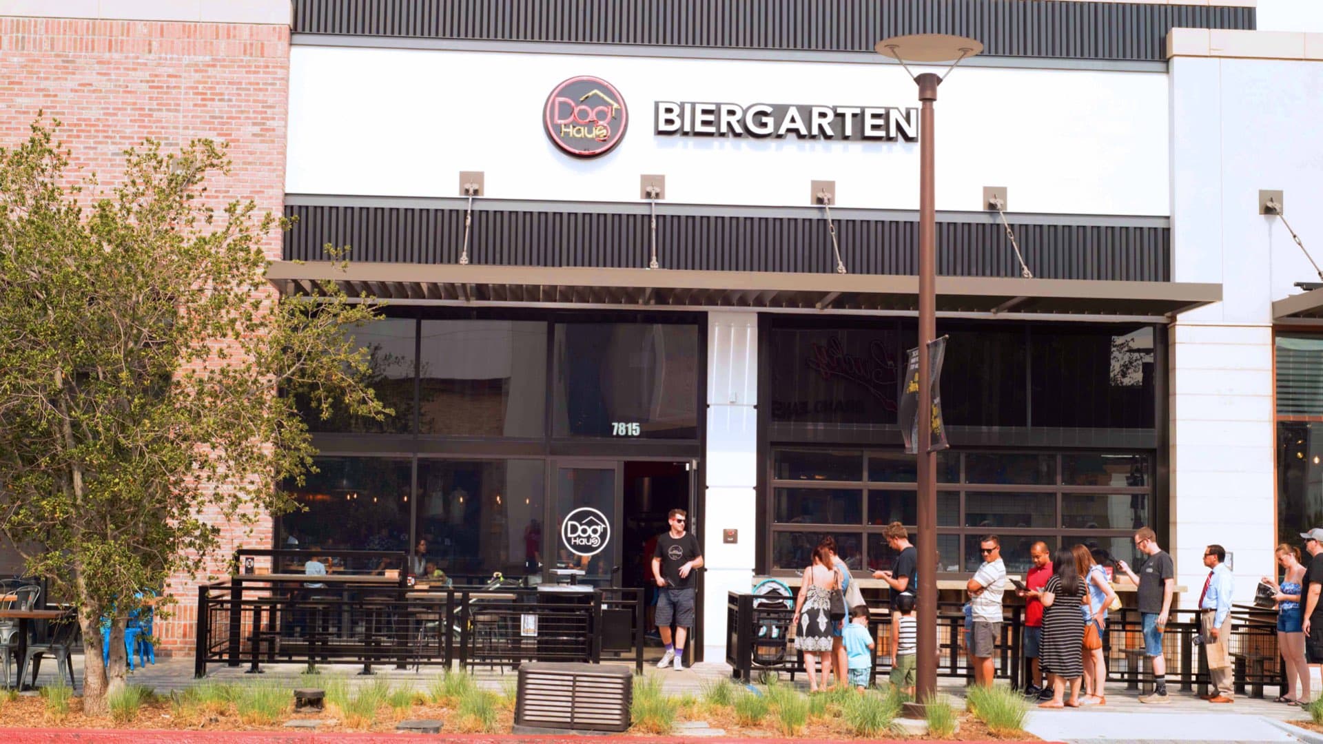 Exterior view of Dog Haus Biergarten in Rancho Cucamonga, featuring a modern storefront with a visible line of customers waiting outside on a sunny day